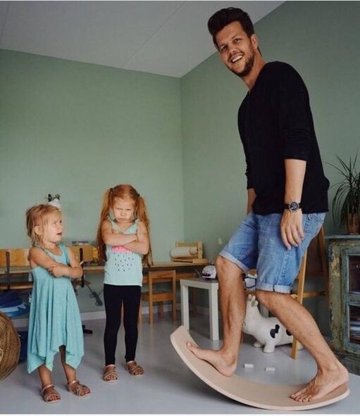 Adult man standing on a Wobbel balance board while two children look on