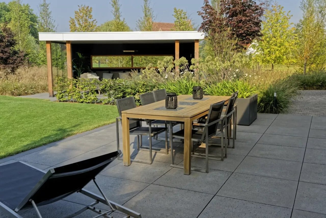 Terras van grote grijze tegels met een tuintafel, gras en een overkapping