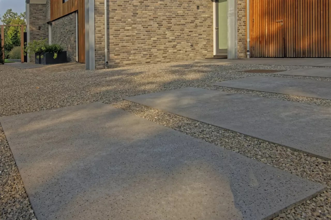 Oprit van grote grijze tegels in grind, voor een garagedeur