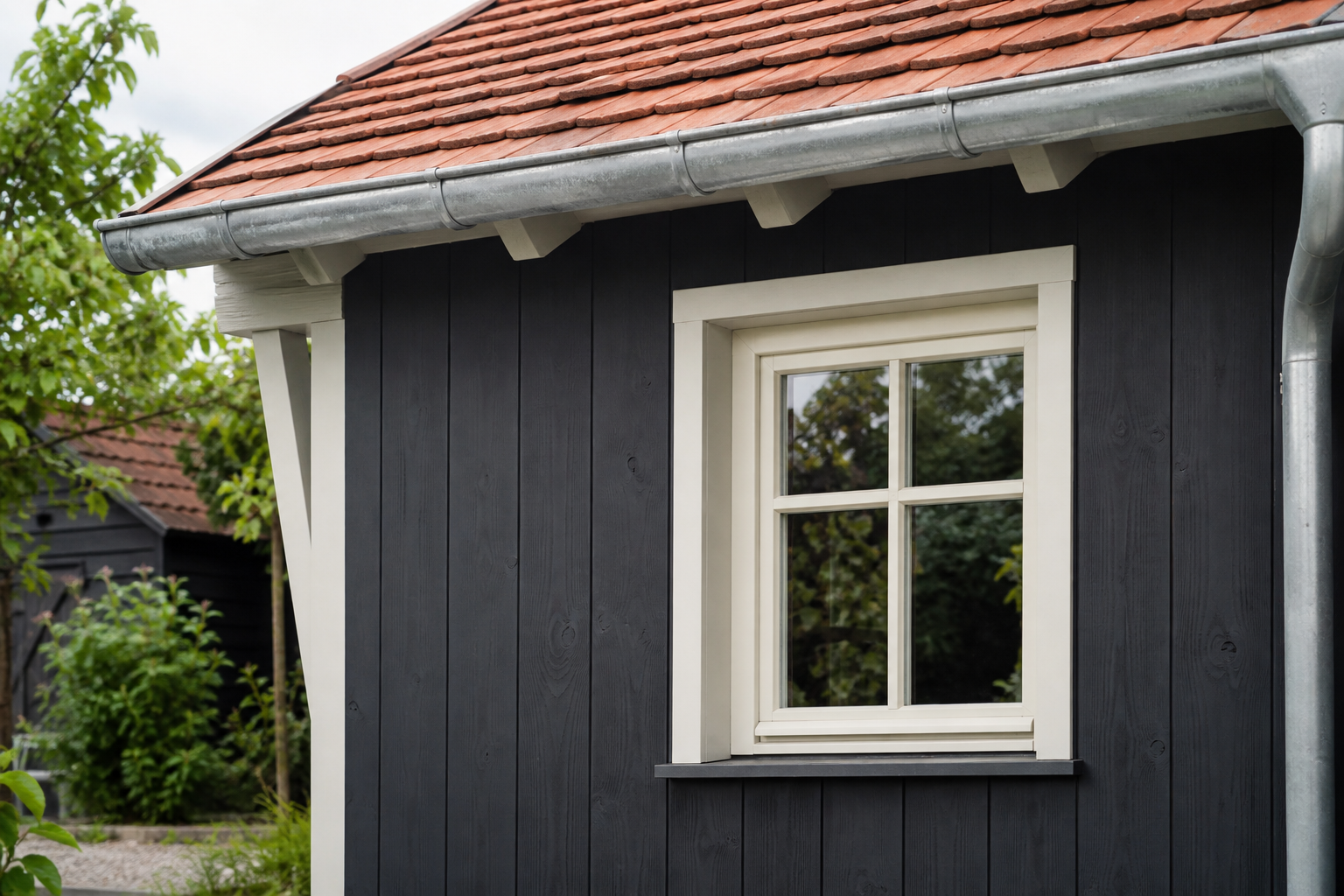 Mattschwarze Holzfassade mit weißem Fenster, Zinkrinne und roten Dachziegeln
