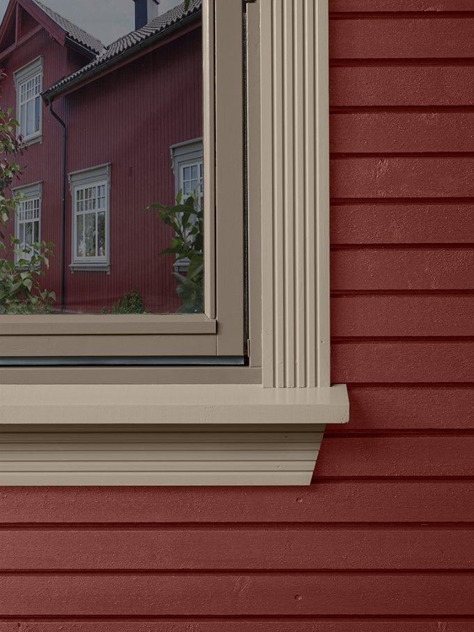 Nahaufnahme eines hell gestrichenen Holzfensterrahmens mit Fensterbank an einer roten Holzfassade