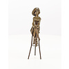 A bronze sculpture of a lady with hat seated on a barstool