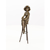 A bronze sculpture of a lady with hat seated on a barstool