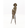 Een bronzen beeld van een dame met hoed gezeten op een barkruk