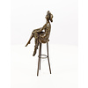 A bronze sculpture of a lady with hat seated on a barstool