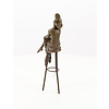 A bronze sculpture of a lady with hat seated on a barstool