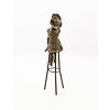 A bronze sculpture of a lady with hat seated on a barstool