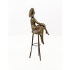 A bronze sculpture of a lady with hat seated on a barstool