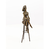 A bronze sculpture of a lady with hat seated on a barstool