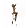 A bronze sculpture of a female nude seated on a barstool