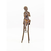 A bronze sculpture of a lady on barstool applying lipstick