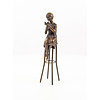 A bronze sculpture of a lady on barstool applying lipstick