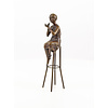 A bronze sculpture of a lady on barstool applying lipstick