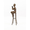 A bronze sculpture of a lady on barstool applying lipstick