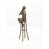 A bronze sculpture of a lady on barstool applying lipstick