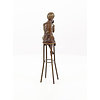 A bronze sculpture of a lady on barstool applying lipstick