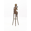 A bronze sculpture of a lady on barstool applying lipstick