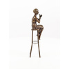 A bronze sculpture of a lady on barstool applying lipstick