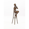 A bronze sculpture of a lady on barstool applying lipstick