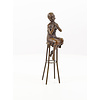 A bronze sculpture of a lady on barstool applying lipstick