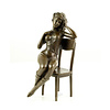 A bronze sculpture of an enticing female seated on a chair