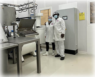 Two workers in white coats pose cheerfully in front of chocolate production machines