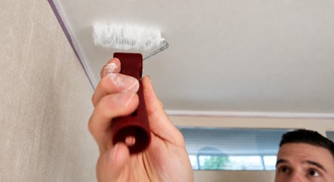 Randen van het plafond schilderen met een kwast en kleine roller
