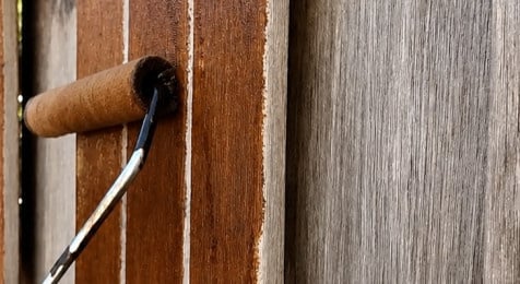 Beits aanbrengen op een houten schutting met kwast en roller
