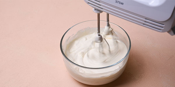 Vanillecreme wird mit Handrührgerät in Glasschüssel geschlagen
