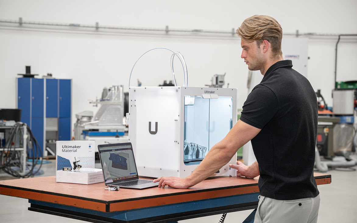 Man kijkt naar een laptop met een 3D print. Ernaast staat een UltiMaker S6