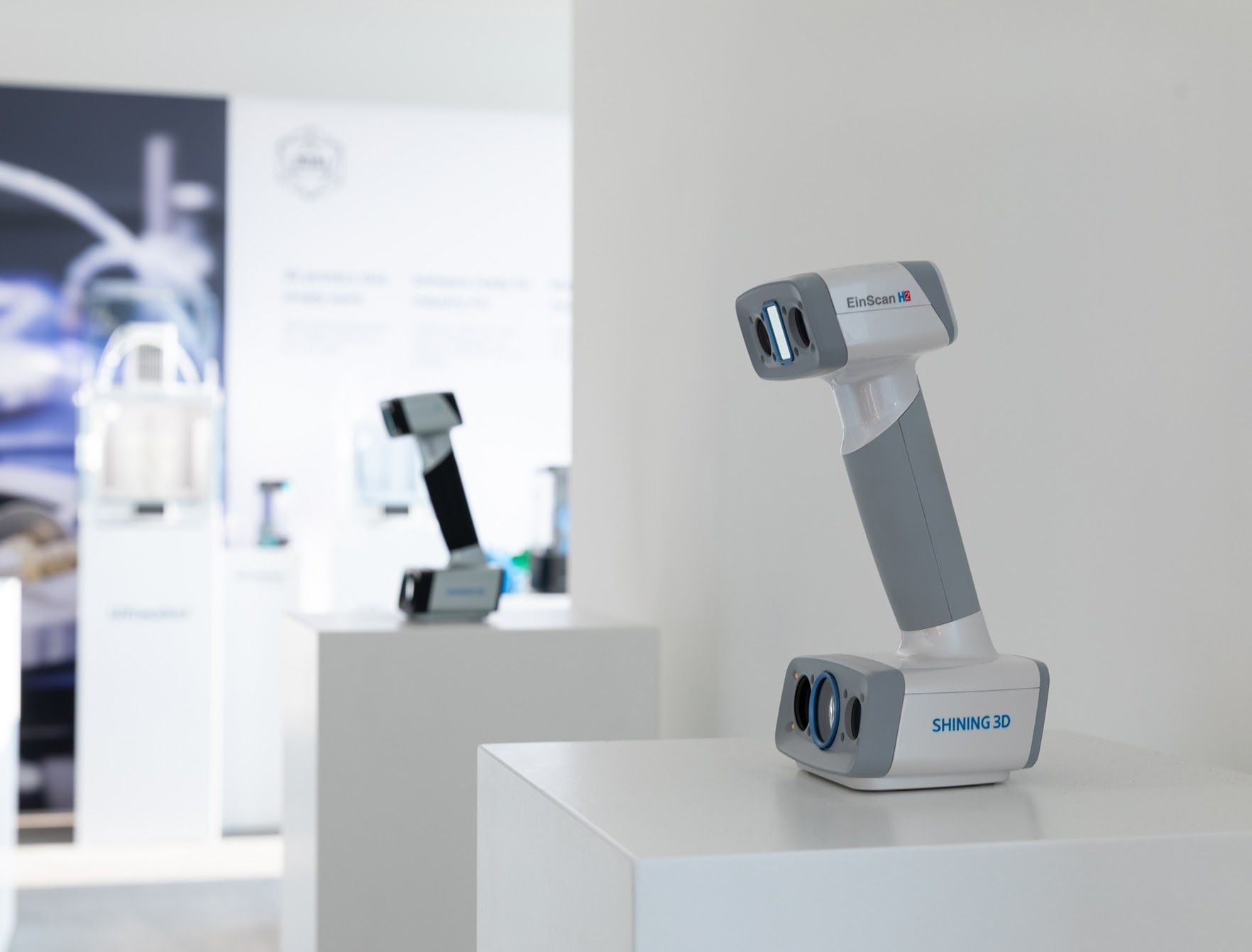 Shining 3D scanner standing on a white pedestal. In the background another 3D scanner is visible.
