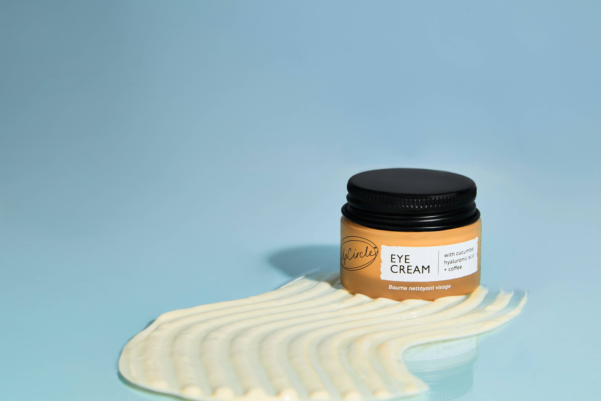 Potje oogcreme op een lichtblauwe achtergrond en een streep van oogcreme