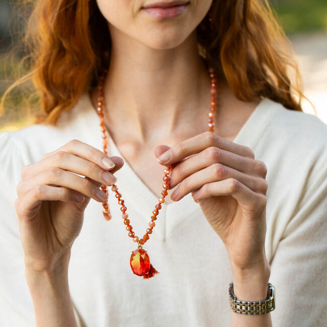 Biba Lange oranje ketting met een glanzende hanger en een kwastje.