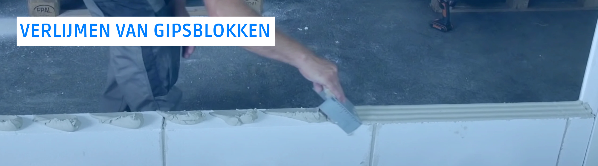 Een bouwvakker brengt gipslijm aan met een troffel/lijmkam op de horizontale en verticale voegen van gipsblokken in halfsteensverband