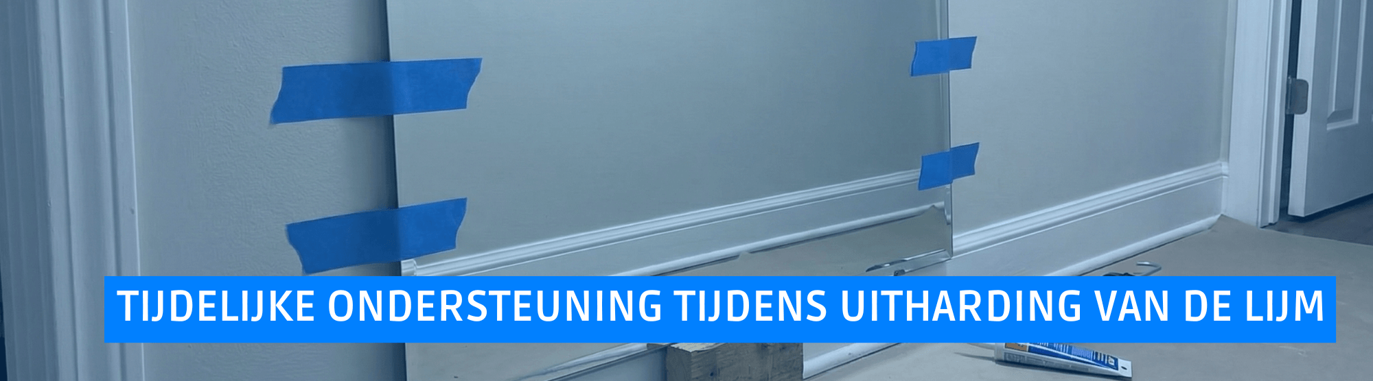 Tijdelijke ondersteuning van een zware spiegel op de muur met behulp van tape en een houten afstandhouder tijdens het uitharden van de lijm.