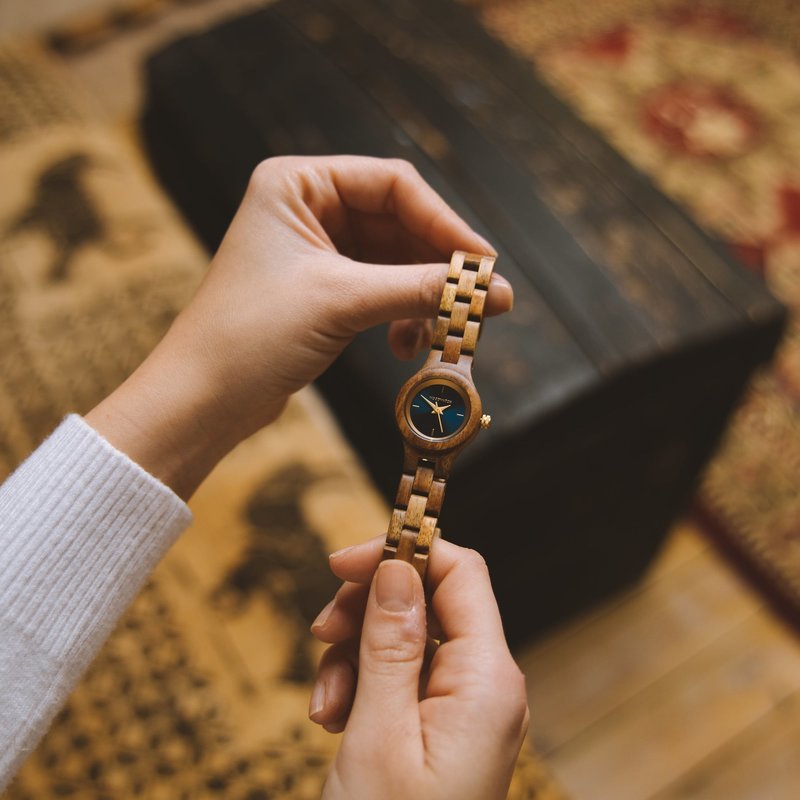 El reloj Bellflower de la Colección FLORA está formado por madera blanda acacia que ha sido formada a mano hasta su más fina esbeltez. El Bellflower cuenta con una esfera azul marino oscuro con detalles de colores dorados.