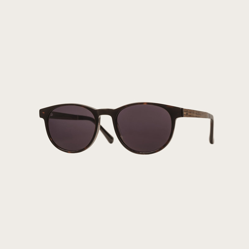 La paire de lunettes l’Ellipse ‘Forever Havanas Black’ poséde un cadre en écaille marron foncé avec des verres noirs. Fabriquée à partir de bois durable et du bioacétate Mazzuchelli Italien avec des branches et écaille de tortue en ébène et manchons en ac