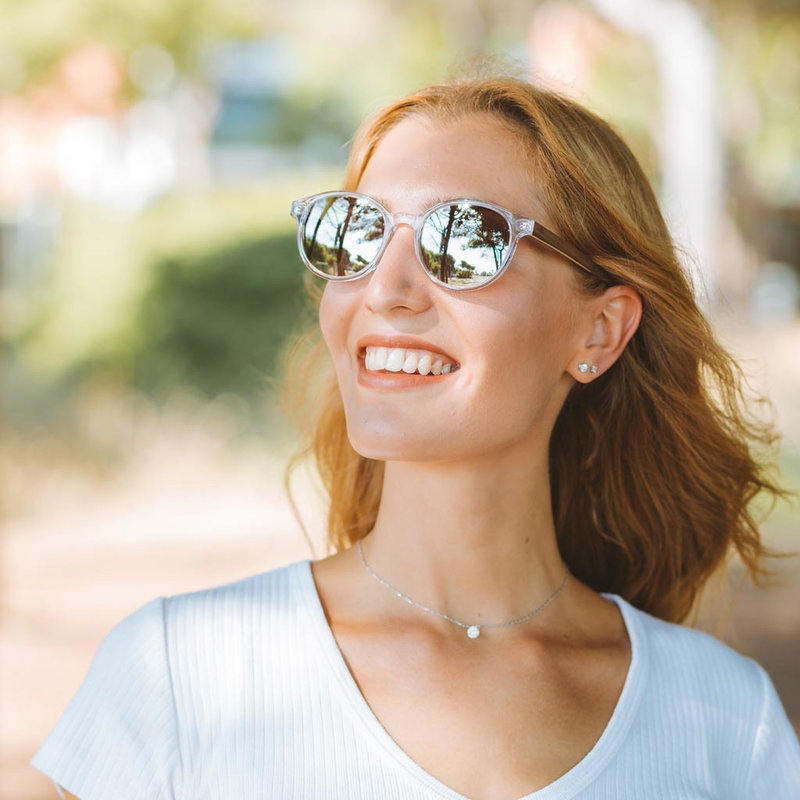 La paire de lunettes le SOHO Clear Smoke poséde un cadre ovale claire avec des verres en gris fumé et fabriquée à partir de bois durable et du bioacétate Mazzuchelli Italien avec des branches de senna siamea naturel en bois et des manchons en acétate nude