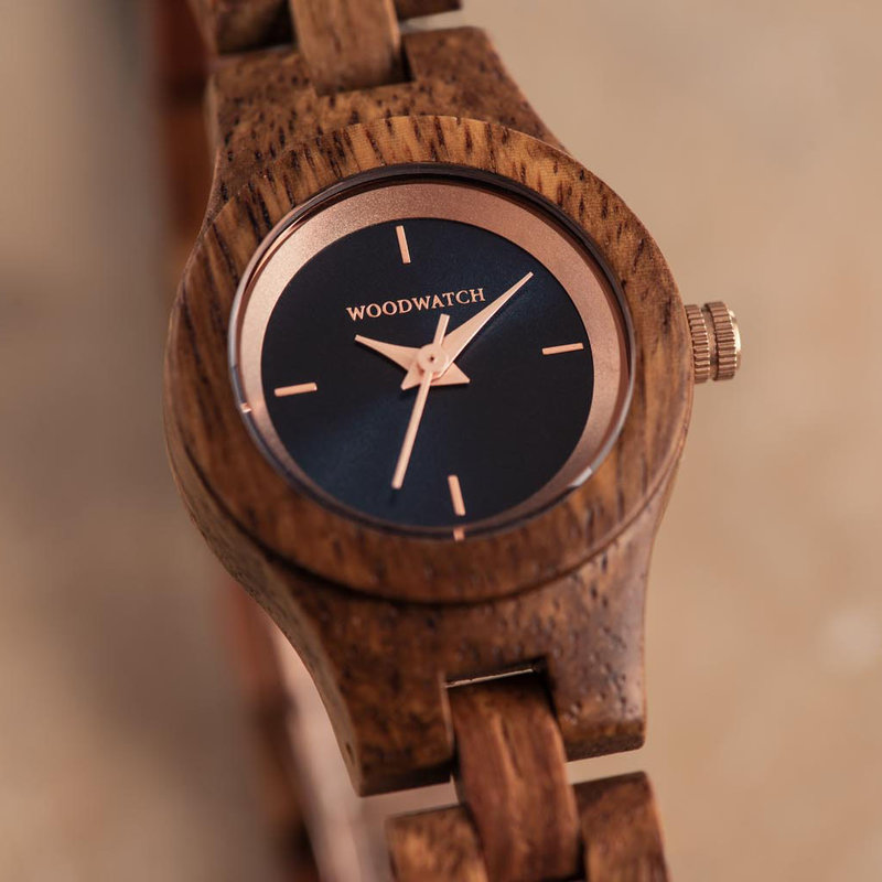 Het Delphine horloge uit de FLORA Collection bestaat uit zacht kosso hout dat met de is hand bewerkt tot een verfijnd uurwerk. De Delphine is voorzien van een donker marineblauwe wijzerplaat met rosé goud accenten.