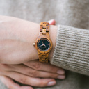 Het Delphine horloge uit de FLORA Collection bestaat uit zacht kosso hout dat met de is hand bewerkt tot een verfijnd uurwerk. De Delphine is voorzien van een donker marineblauwe wijzerplaat met rosé goud accenten.