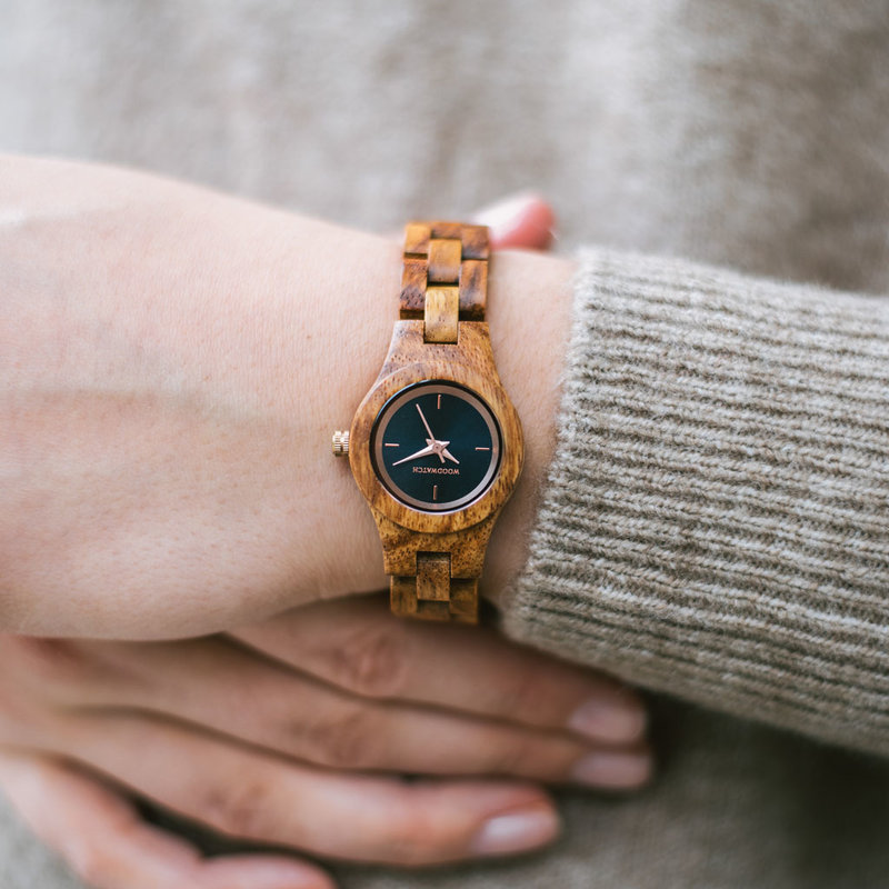 La montre Delphine de la collection FLORA est composée de bois lisse kosso finement travaillé à la main. Le modèle Delphine comporte un cadran bleu marine foncé avec des détails colorés or rose.