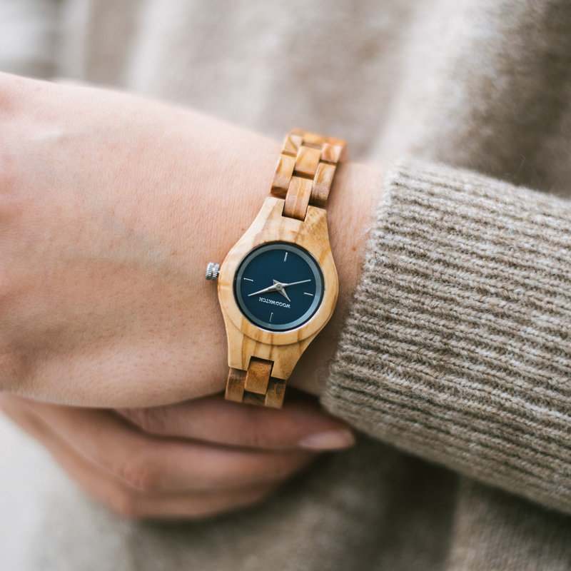 El reloj Iris de la Colección FLORA está formado por madera de olivo blanda que ha sido formada a mano hasta su más fina esbeltez. El reloj Iris cuenta con una esfera azul nocturno con detalles en colores plata.