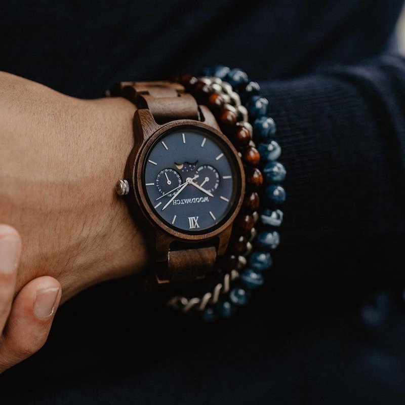 CLASSIC Sailor har en elegant smal boett samtidigt som den har en unik månfasrörelse och två extra urtavlor. Klockan är tillverkad av östafrikanskt kossoträ och är försedd med en blå urtavla och gyllene detaljer. Matcha den perfekt med ELLIPSE Clear BlueB