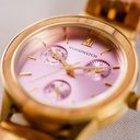 La Radiance Rose Champagnee est en bois d'olivier et en acier inoxydable brossé or, complétée par un cadran rose clair et des détails en métal brossé or.