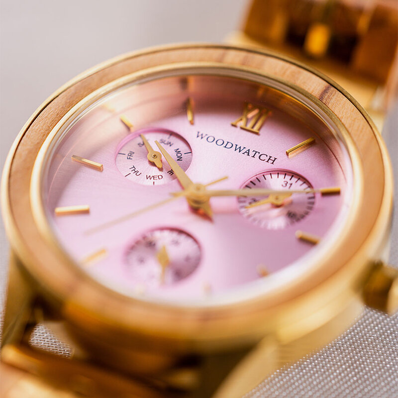 La Radiance Rose Champagnee est en bois d'olivier et en acier inoxydable brossé or, complétée par un cadran rose clair et des détails en métal brossé or.