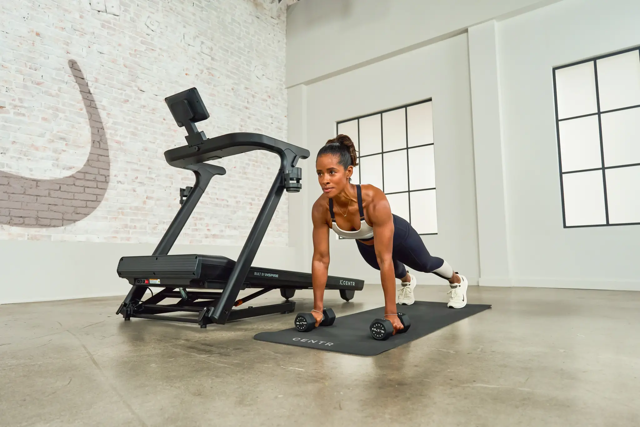Vrouw in een plank houding met dumbbells waaraan ze vasthoudt