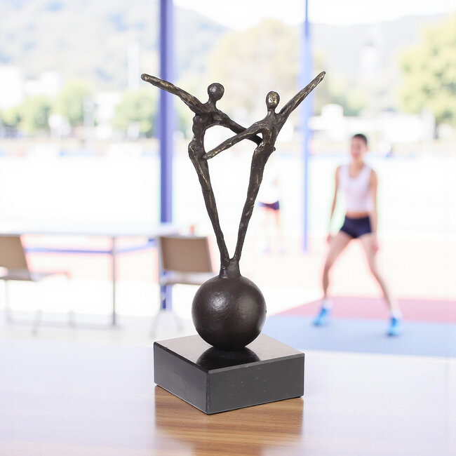 Ger van Tankeren Topprestatie. Twee verbronsde figuren op een bolsculptuur.