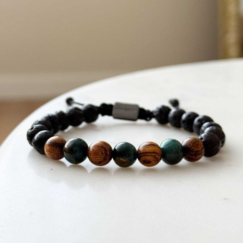 Made with rosewood beads, volcanic beads, dark green natural stone beads, and a matte black brass closure. Adjustable, with 8mm beads to fit most wrist sizes.