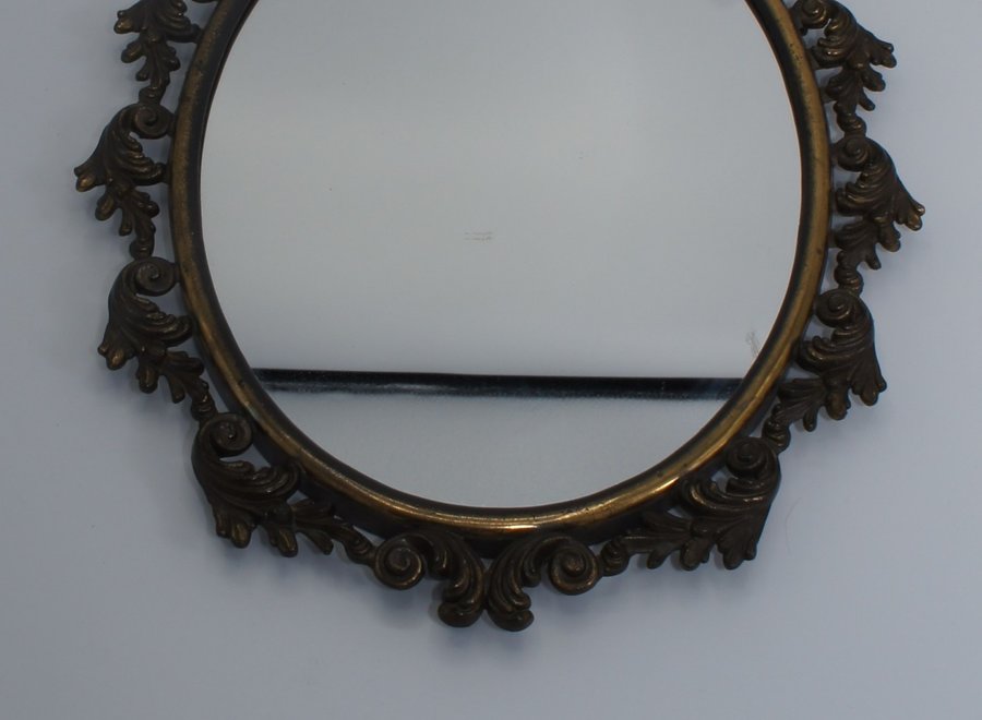 Beautiful ornate oval bronze mirror, decorated with curls.
