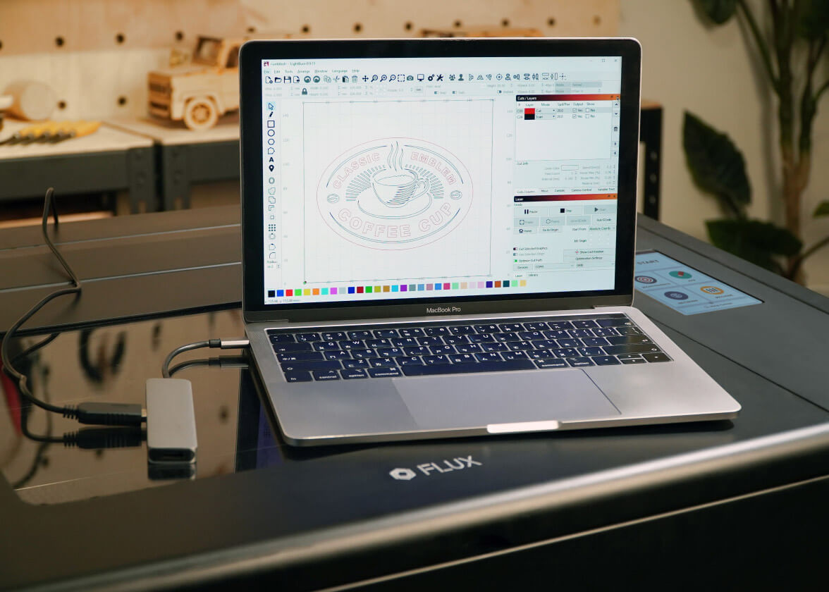 Laptop with the LightBurn software on top of a FLUX Beambox, connected with a LightBurn bridge cable